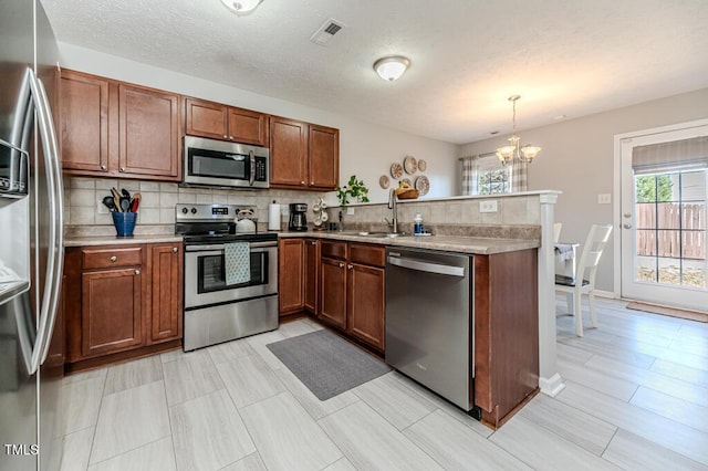 kitchen featuring pendant lighting, appliances with stainless steel finishes, an inviting chandelier, decorative backsplash, and sink