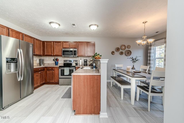 kitchen featuring an inviting chandelier, stainless steel appliances, tasteful backsplash, decorative light fixtures, and sink