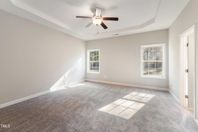 empty room with ceiling fan, a tray ceiling, and light carpet