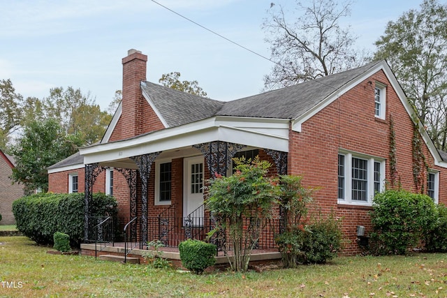 view of front of property featuring a front yard, covered porch, brick siding, and a chimney