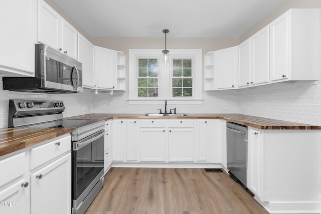 kitchen featuring open shelves, butcher block counters, stainless steel appliances, and a sink