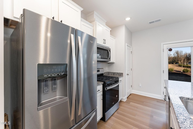 kitchen featuring appliances with stainless steel finishes, light wood-type flooring, white cabinets, and light stone countertops