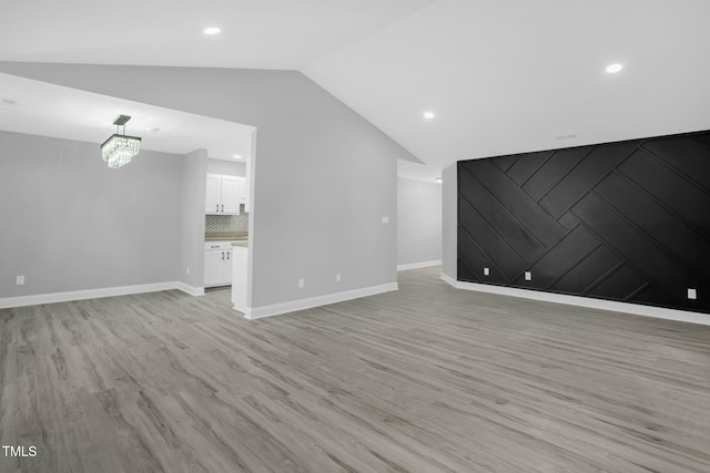 unfurnished living room featuring lofted ceiling, a notable chandelier, and light hardwood / wood-style floors