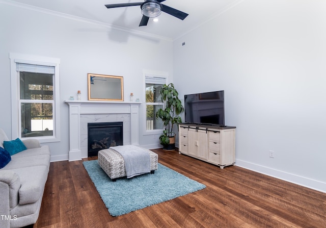 living room featuring ceiling fan, a tiled fireplace, dark hardwood / wood-style flooring, and crown molding