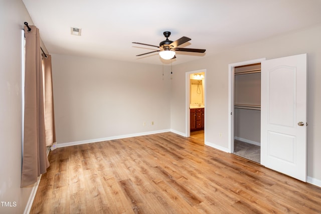 unfurnished bedroom with ensuite bathroom, a walk in closet, a closet, ceiling fan, and light hardwood / wood-style floors