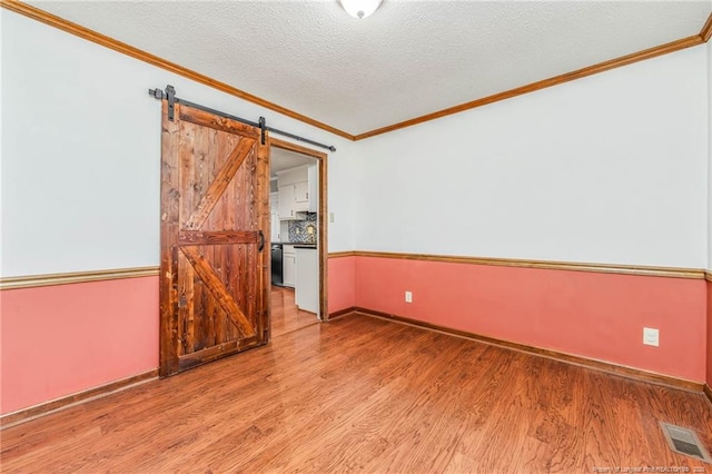 spare room featuring light hardwood / wood-style floors, crown molding, a barn door, and a textured ceiling