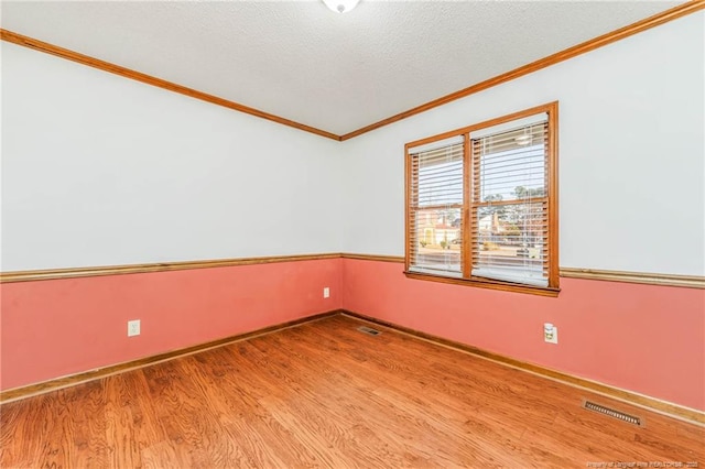 empty room with a textured ceiling, hardwood / wood-style floors, and crown molding