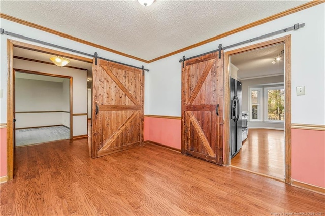 unfurnished room featuring a textured ceiling, a barn door, crown molding, and hardwood / wood-style floors