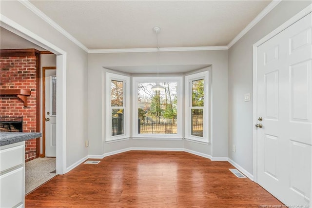 unfurnished dining area featuring hardwood / wood-style floors, crown molding, and a fireplace