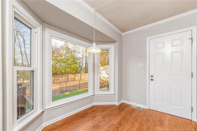 unfurnished dining area featuring a textured ceiling, hardwood / wood-style floors, and crown molding