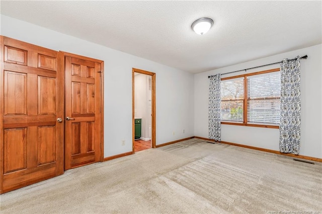 unfurnished bedroom with ensuite bathroom, a textured ceiling, and light colored carpet