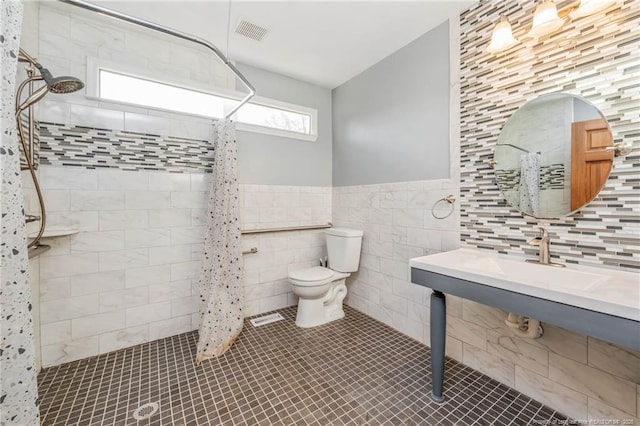 bathroom featuring toilet, tiled shower, tile walls, and tile patterned floors