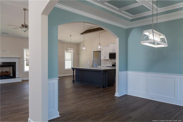 kitchen featuring hanging light fixtures, a center island with sink, white cabinets, ceiling fan, and beamed ceiling