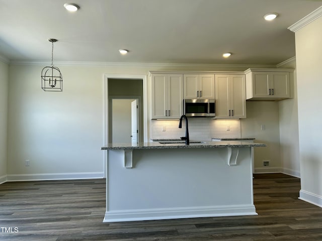 kitchen featuring stone counters, a center island with sink, stainless steel microwave, white cabinets, and a sink