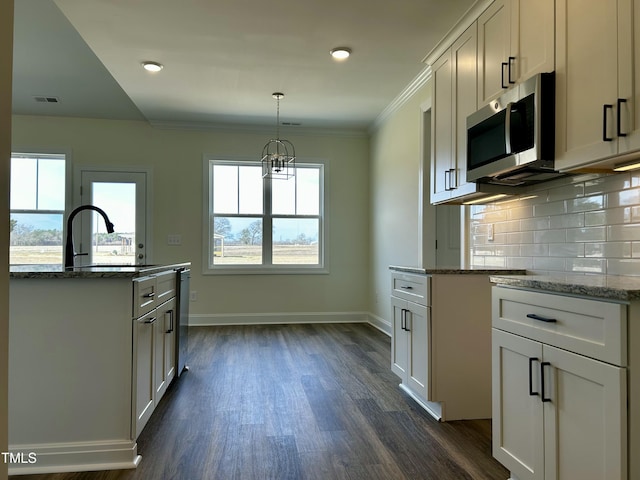 kitchen with light stone counters, stainless steel appliances, a sink, white cabinets, and hanging light fixtures