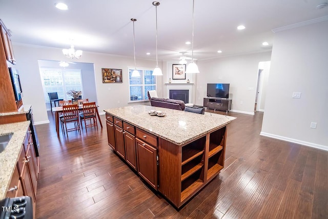 kitchen featuring crown molding, a fireplace, a center island, and light stone countertops