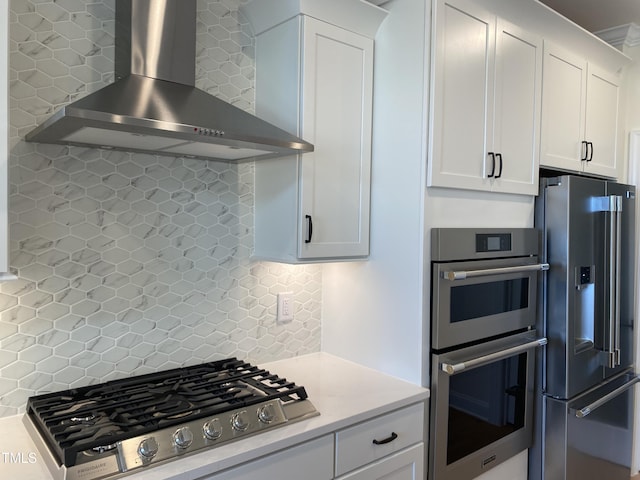 kitchen with wall chimney range hood, backsplash, white cabinetry, and appliances with stainless steel finishes