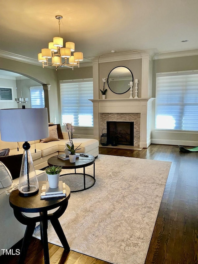 living room featuring a chandelier, crown molding, dark hardwood / wood-style floors, and a stone fireplace