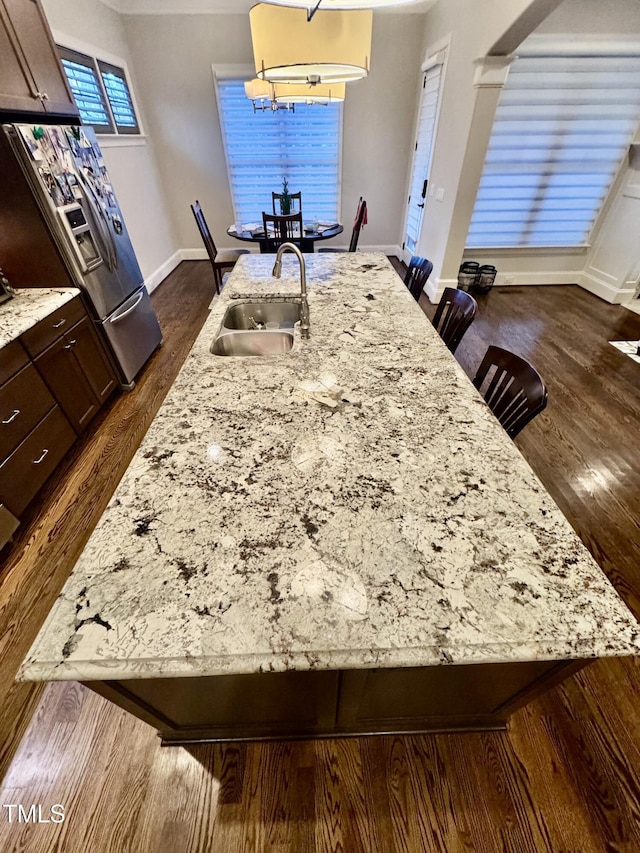 details featuring stainless steel refrigerator with ice dispenser, dark brown cabinetry, a breakfast bar, and sink