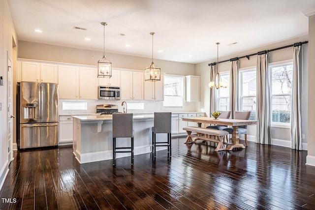 kitchen featuring pendant lighting, stainless steel appliances, an island with sink, white cabinets, and a kitchen bar