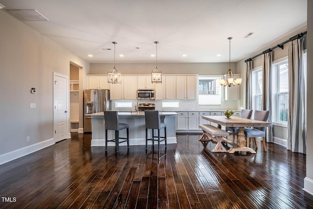 kitchen with stainless steel appliances, a breakfast bar, a kitchen island with sink, and hanging light fixtures