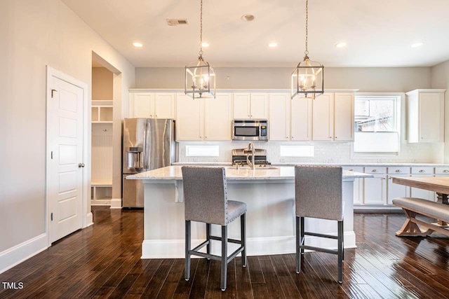 kitchen featuring white cabinetry, stainless steel appliances, an island with sink, dark hardwood / wood-style flooring, and decorative light fixtures