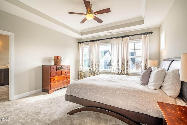 carpeted bedroom featuring ensuite bath, ornamental molding, and a tray ceiling