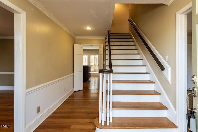 stairway with recessed lighting, wood finished floors, wainscoting, and crown molding