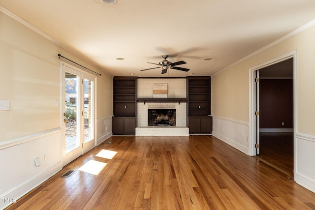 unfurnished living room featuring visible vents, built in features, ornamental molding, a fireplace, and wood finished floors