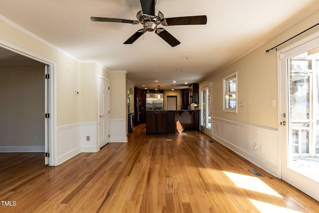 unfurnished living room featuring visible vents, crown molding, a wainscoted wall, and wood finished floors