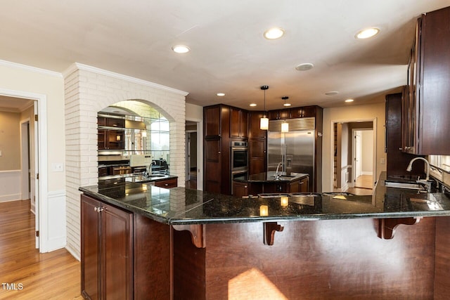 kitchen featuring light wood-style flooring, stainless steel built in refrigerator, a sink, wainscoting, and crown molding