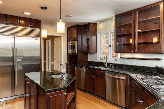 kitchen featuring light wood finished floors, built in appliances, dark stone counters, and a sink