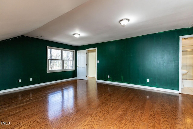 empty room featuring visible vents, baseboards, wood finished floors, and vaulted ceiling