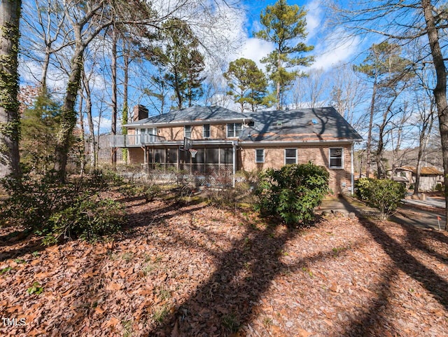 rear view of property with brick siding, a chimney, and a sunroom