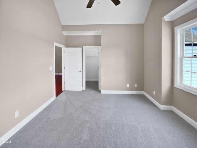 unfurnished bedroom featuring ceiling fan, a spacious closet, light carpet, and vaulted ceiling