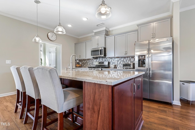 kitchen featuring pendant lighting, appliances with stainless steel finishes, and a kitchen island with sink