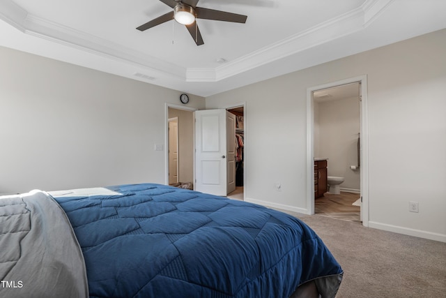 bedroom featuring ensuite bathroom, ceiling fan, a tray ceiling, a walk in closet, and a closet