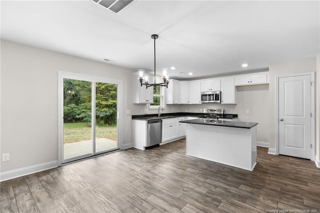 kitchen with stainless steel appliances, a center island, dark wood-type flooring, white cabinetry, and decorative light fixtures