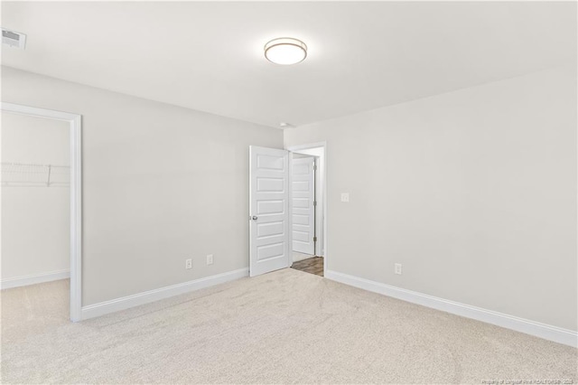 unfurnished bedroom with light colored carpet, a closet, and a spacious closet