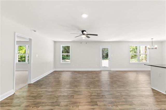 empty room with ceiling fan with notable chandelier, dark hardwood / wood-style flooring, and plenty of natural light