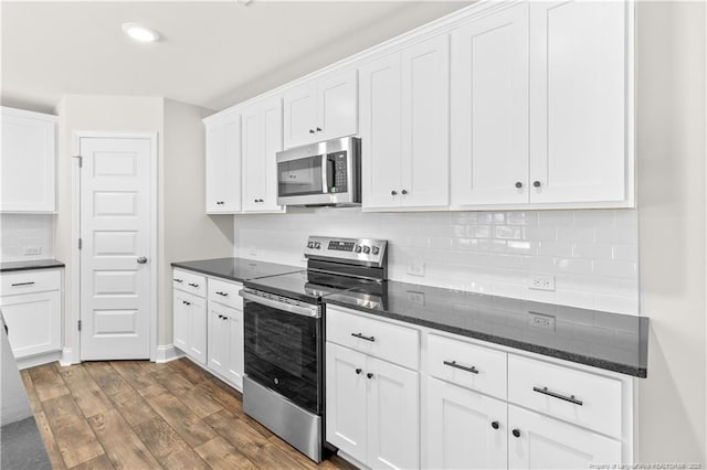 kitchen featuring appliances with stainless steel finishes, white cabinetry, dark stone countertops, and backsplash