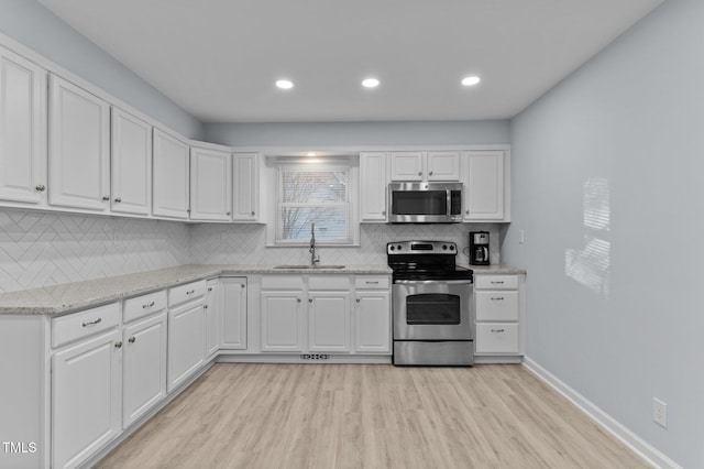 kitchen featuring appliances with stainless steel finishes, sink, white cabinets, light stone countertops, and light hardwood / wood-style flooring