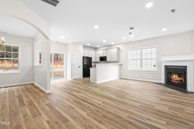 unfurnished living room featuring a wealth of natural light, ceiling fan with notable chandelier, and light hardwood / wood-style flooring