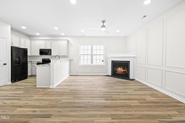 kitchen with black appliances, white cabinetry, kitchen peninsula, light wood-type flooring, and ceiling fan