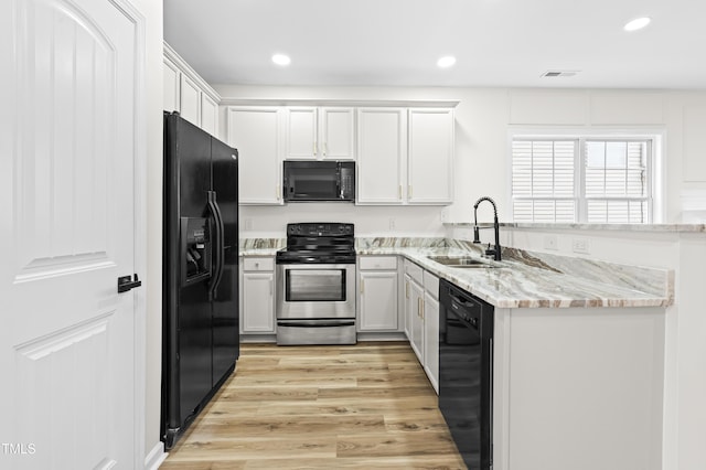 kitchen with light stone counters, sink, white cabinets, and black appliances