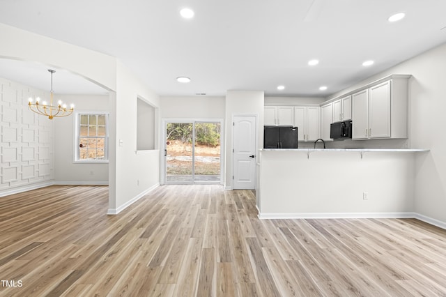 kitchen with black appliances, white cabinetry, light hardwood / wood-style floors, kitchen peninsula, and a notable chandelier