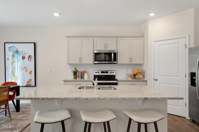 kitchen with light stone countertops, stainless steel appliances, a center island with sink, decorative backsplash, and white cabinetry