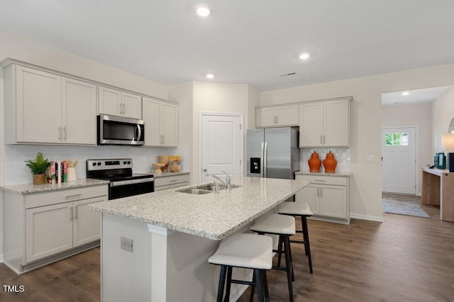 kitchen with light stone countertops, a center island with sink, a breakfast bar, appliances with stainless steel finishes, and sink