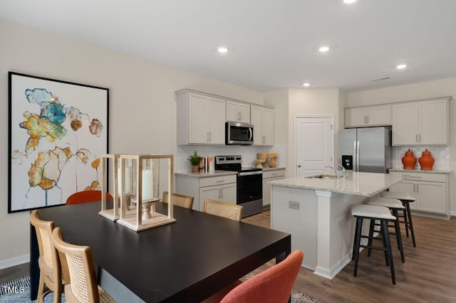 kitchen with stainless steel appliances, sink, white cabinets, tasteful backsplash, and an island with sink