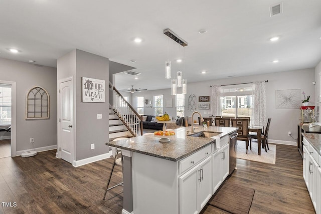 kitchen with stainless steel dishwasher, a kitchen island with sink, white cabinets, dark stone counters, and sink